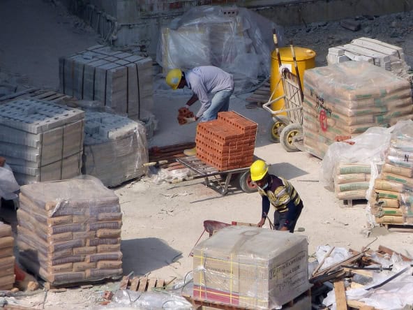 Construction workers on a site with bricks, cement bags, and building tools.